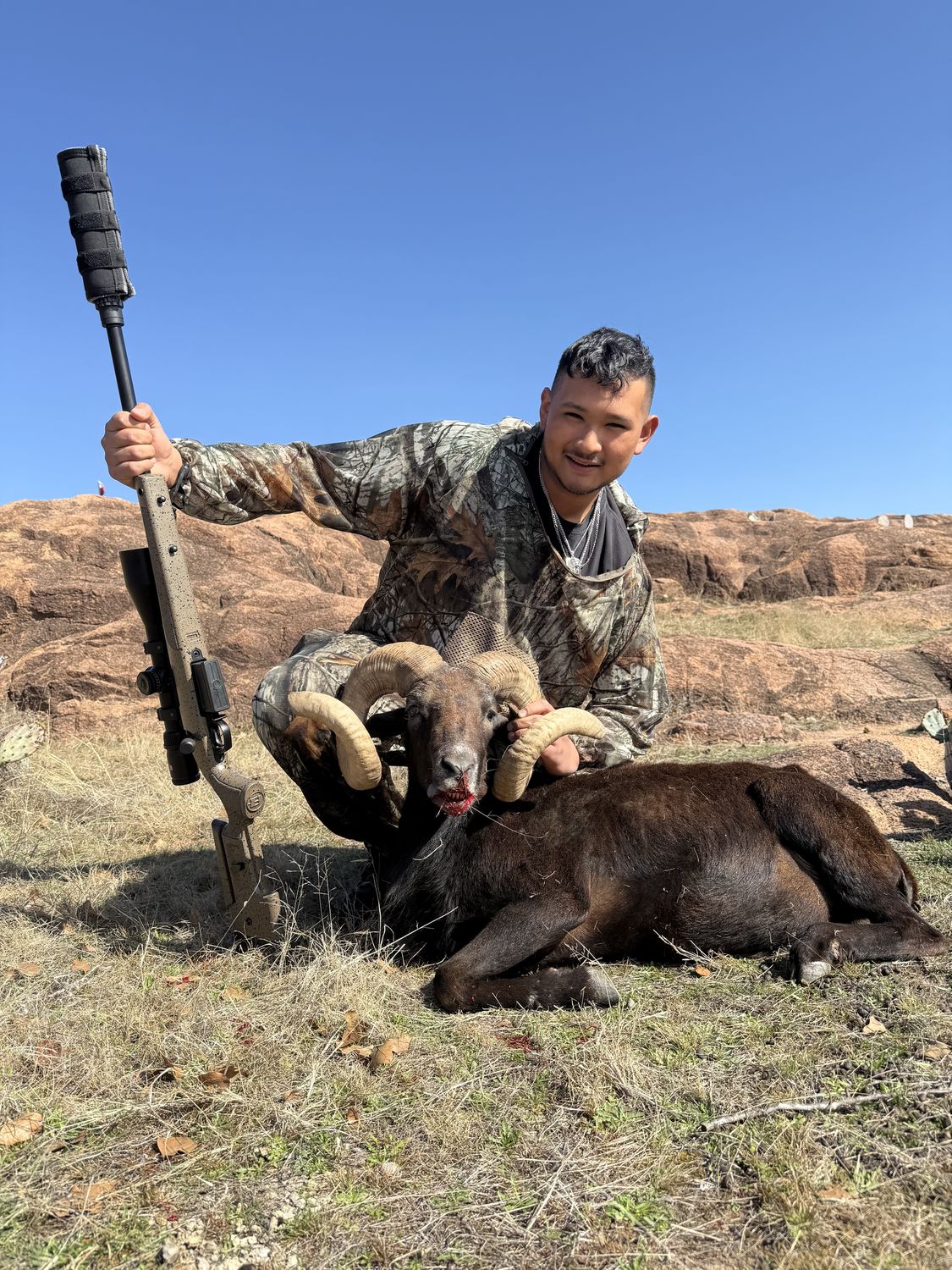 A young hunter with a black Hawaiian ram on the granite